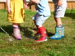 Three young children splashing in puddles in the garden at Juniors Day Nursery.