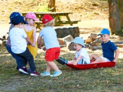 Pre-school children playing with a sledge in the garden at Juniors Day Nursery.