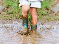 Young child splashing in muddy puddles in the garden at Juniors Day Nursery.